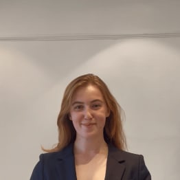 Smiling person with long auburn hair wearing a dark blazer against a plain white background. The tone is professional and approachable.