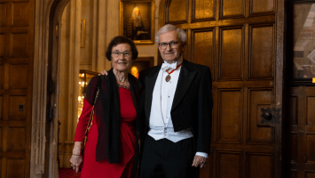 Sir Geoffrey Vos wearing white tie dress, poses with his arm around his wife (who wears a red evening gown), in the Upper Vestibule at Lincoln's Inn