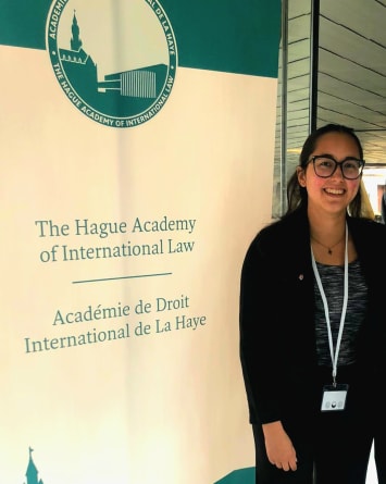 Natasha King stands in front of 'The Hague Academy of International Law' banner