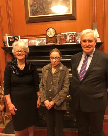 Members of Lincoln's Inn stand either side of Ruth Bader Ginsburg, the late US Supreme Court Judge. Ruth Bader Ginsburg wears a grey patterned jacket and black glasses.