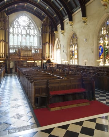 Empty chapel with dark wooden pews. The floor is laid with linoleum in a pattern which features black and white diamonds in an alternating fashion.