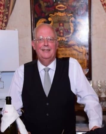 Photograph of Tony Payne a Butler at the Inn. He is dressed on white shirt, tie and black waistcoat and is stood at the Bar in the Old Hall.