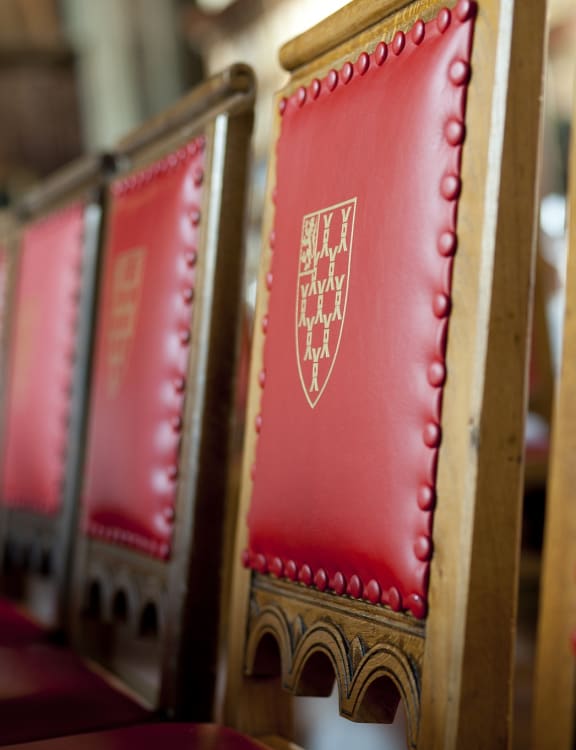 A row of wooden chairs with red leather backs and the gold crest of Lincoln's Inn on the centre of them