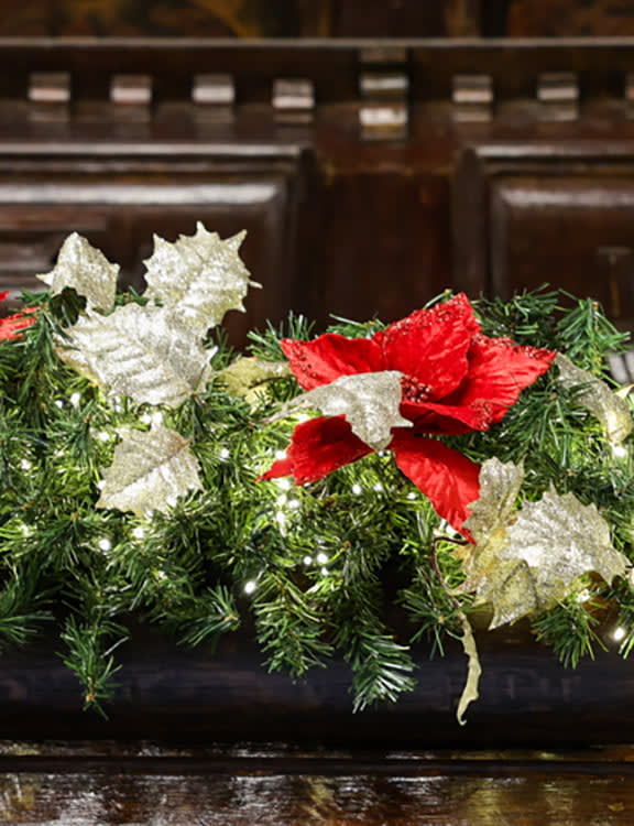 Festive garland with red poinsettias, glittery silver leaves, and soft white lights on dark wood, conveying a warm holiday atmosphere.