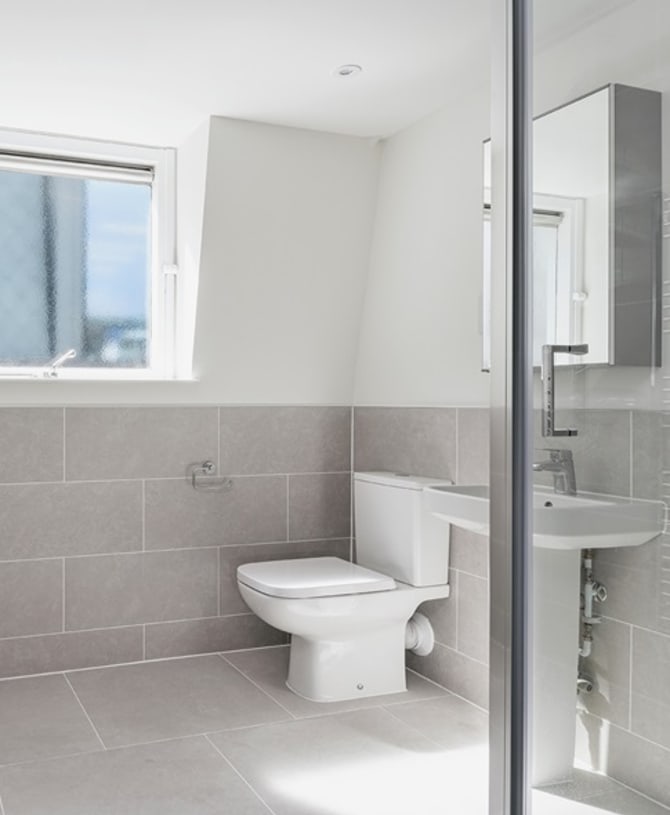 Photograph of modern bathroom with grey tiling, white porcelain toilet and window with frosted glass.