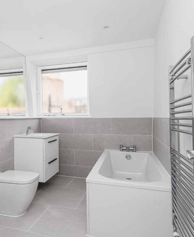 Modern bathroom featuring grey tiling, a transparent walk in shower and white toilet, basin and sink (with drawers below).
