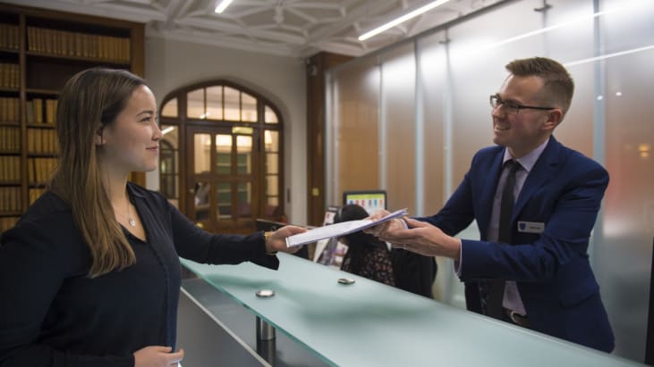 A woman in Lincoln's Inn recpetion hands over a document to a man on the reception desk