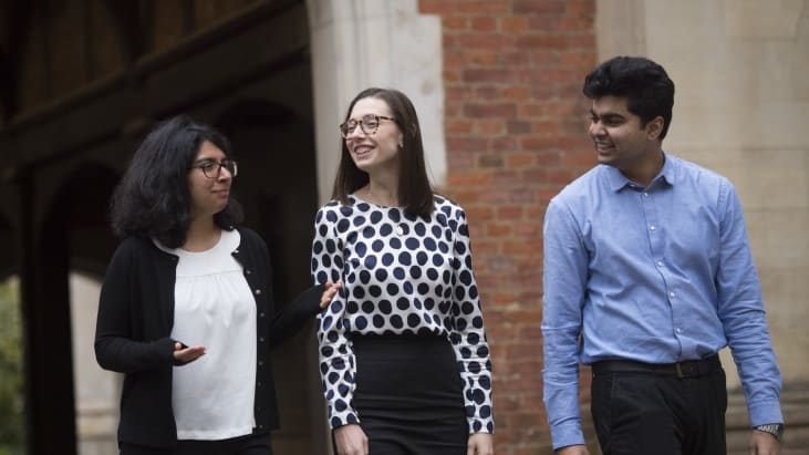 Two women and a man in smart professional clothing walk under a stone archway at Lincoln's Inn