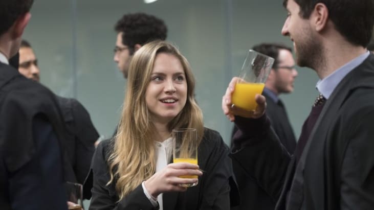 Attendees dressed in formal attire enjoy glasses of orange juice at an event.