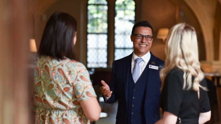 Blonde woman and brown haired woman being welcomed to the MCR by man in blue suit
