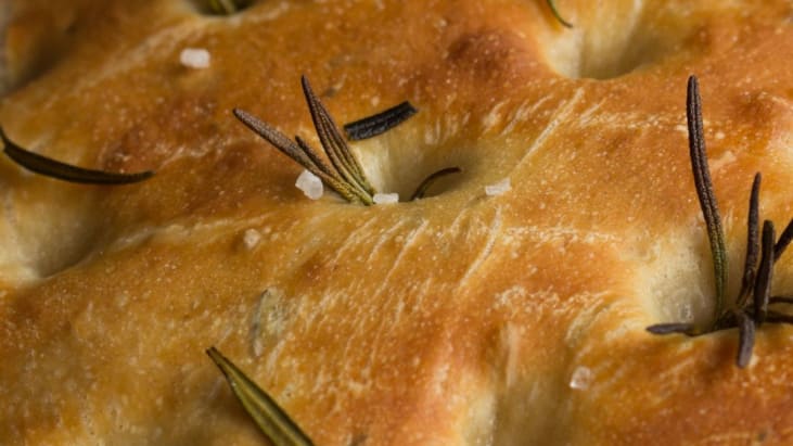A close up of golden focaccia bread sprinkled with sea salt and sprigs of rosemary