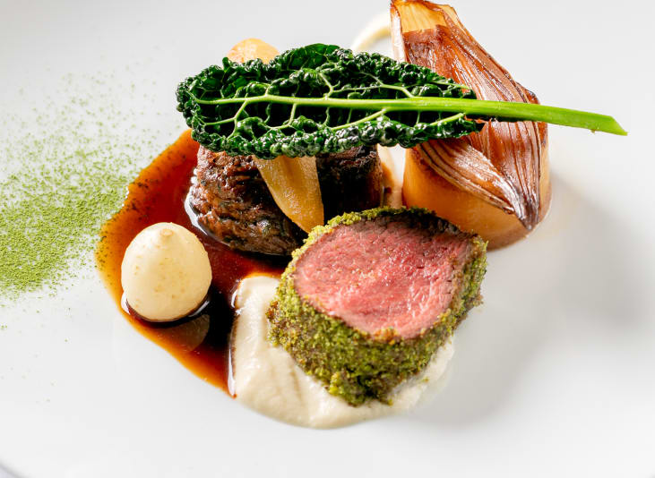 Fine dining dish consisting of a cut of steak, greens and a rich sauce