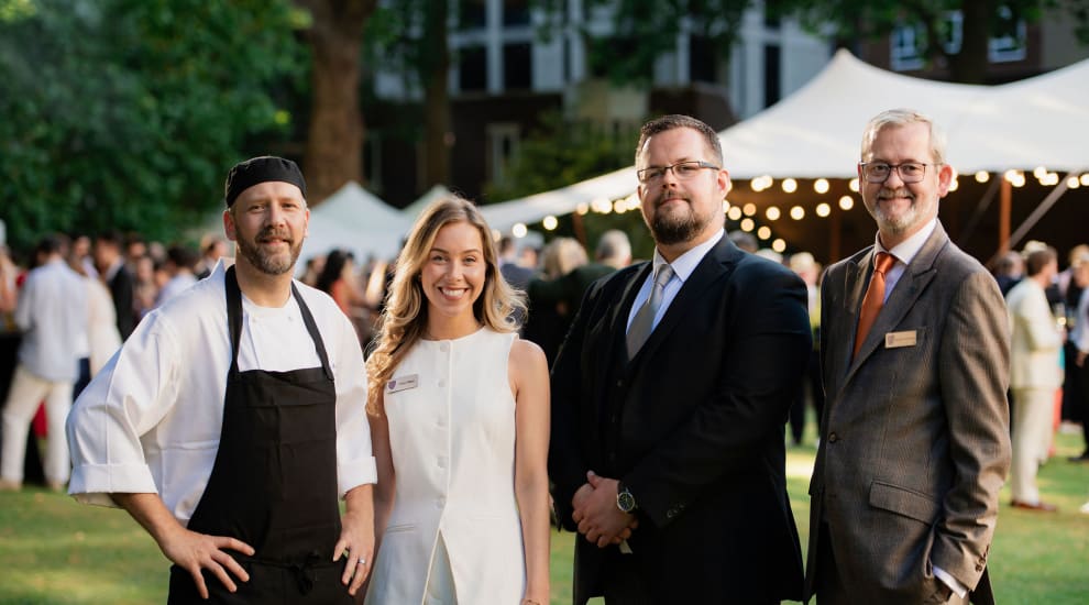 Four people smiling from the lincoln's inn front of house team. The photo is taken in the gardens of Lincon's Inn at the annual garden party. The photo is of the senior management from the catering department at lincoln's inn - a chef, front of house manager, head of sales and head of catering department