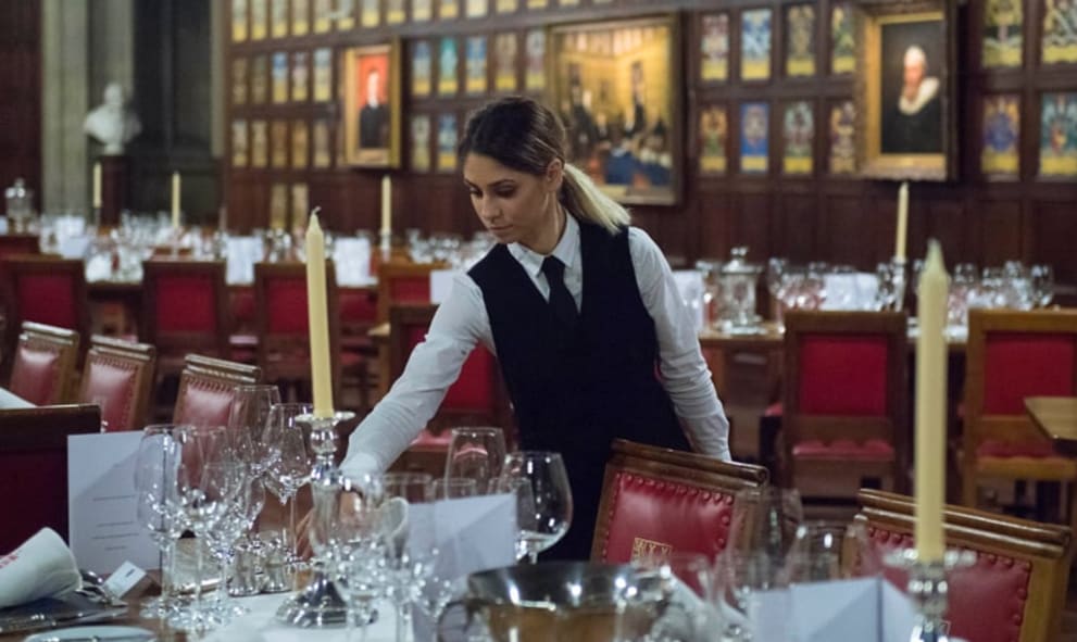 Member of staff setting up tables for dinner in historic hall