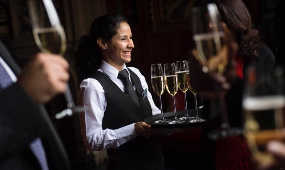 Member of staff serving a tray of drinks to guests in historic hall