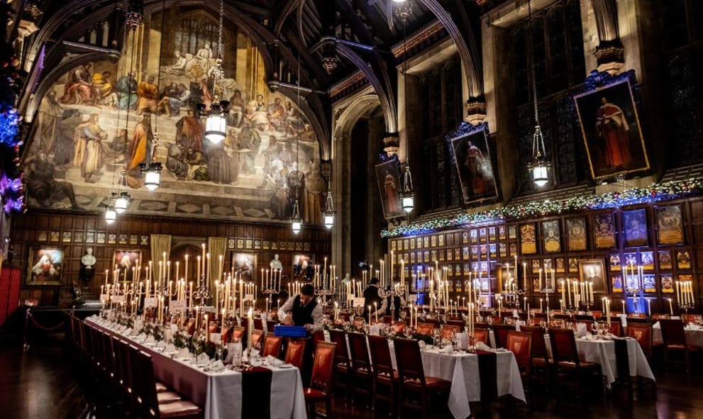Great Hall at Christmas laid for a banquet and candlelit. Decorated with fairy lit garlands and wreaths