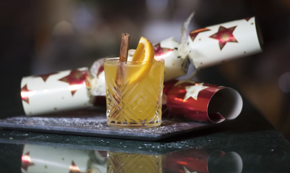 Red an white crackers on a platter behind an orange and cinnamon cocktail in a whisky glass