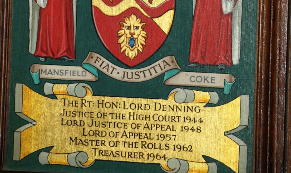 A wooden frame displaying The Rt Hon Lord Denning's coat of arms, featuring two figures in red robes holding a shield.