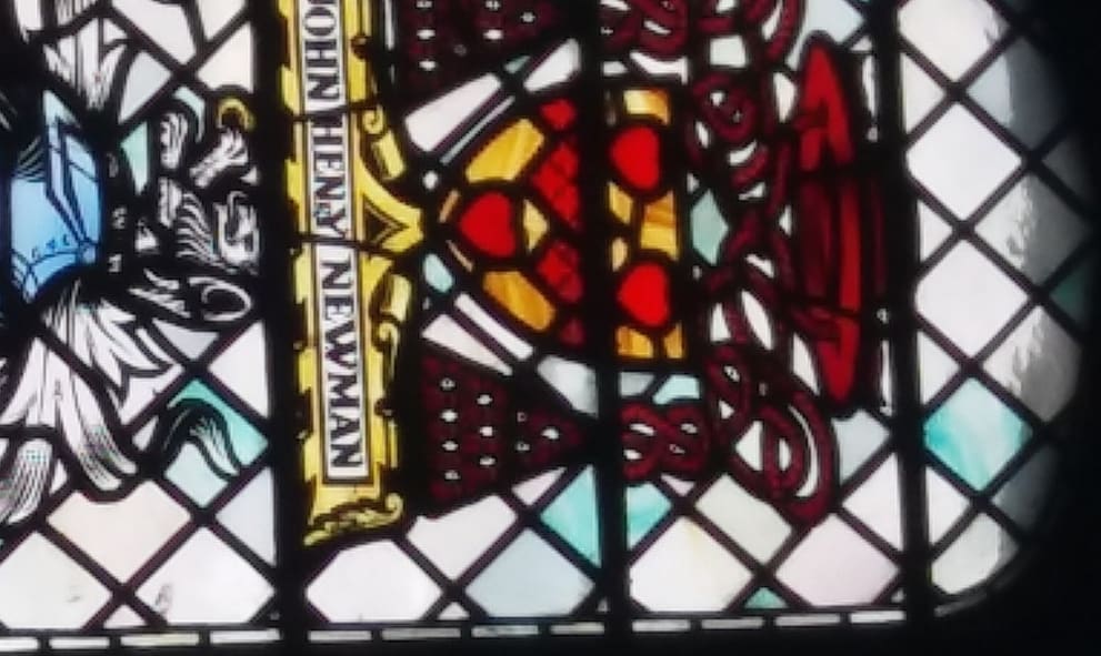 Stained glass window decorated with the heraldic panel of John Newman. The design features a shield with shades of red.