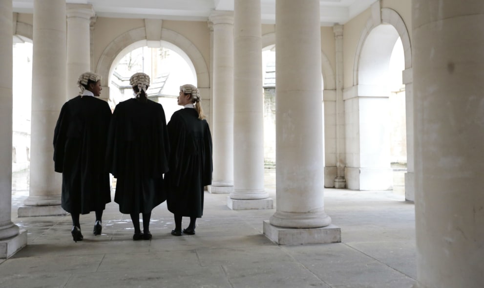 Barristers in wigs and gowns stand in an archway, surrounded by brick columns