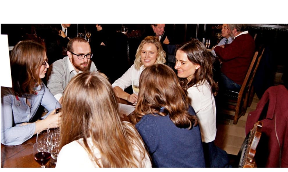 Group photo of quiz contestants talking at a table, laid with empty wine glasses.
