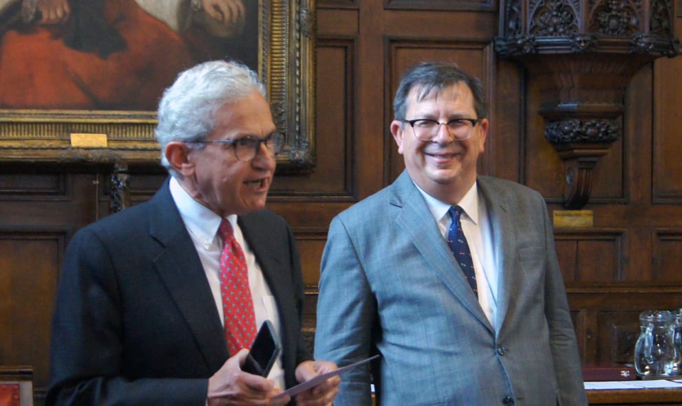 The Treasurer, in black suit and red tie, introducing The Hon Andrew Bell, in grey suit and blue tie, to Hall on the wood paneled dias in Lincoln's Inn Great Hall