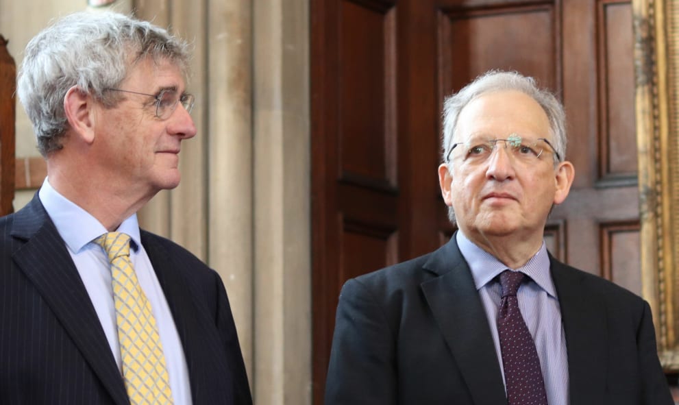 Sir Jon Cunliffe stands next to the Treasurer (The Rt Hon Lord Briggs of Westbourne) in the Great Hall of Lincoln's Inn. Sir Jon Cunliffe is an older white man, dressed in rimless spectacles, dark suit blazer and a lilac suit with an accompanying tie.