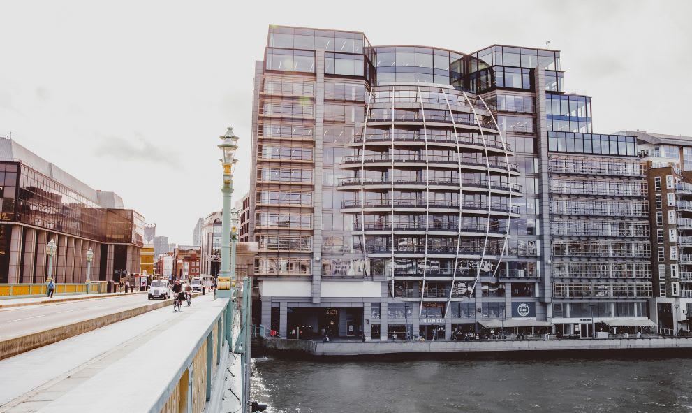 The exterior of the Ofcom offices, Riverside House, London. A large modern, curved, glass building. The building is across an old bridge on the river Thames.