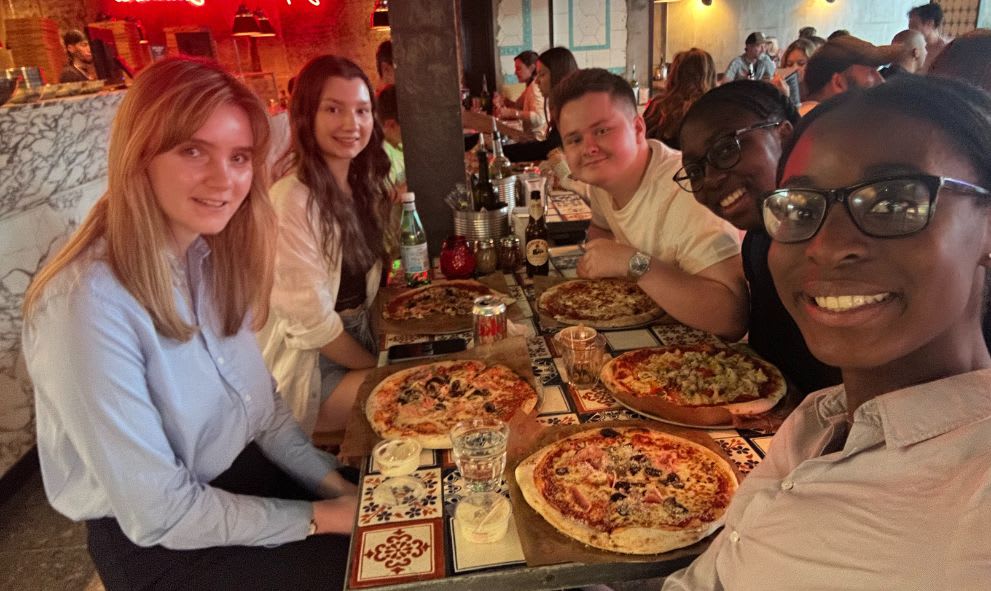 Attendees of the summer school sitting a table in a casual pizza restaurant having pizza.