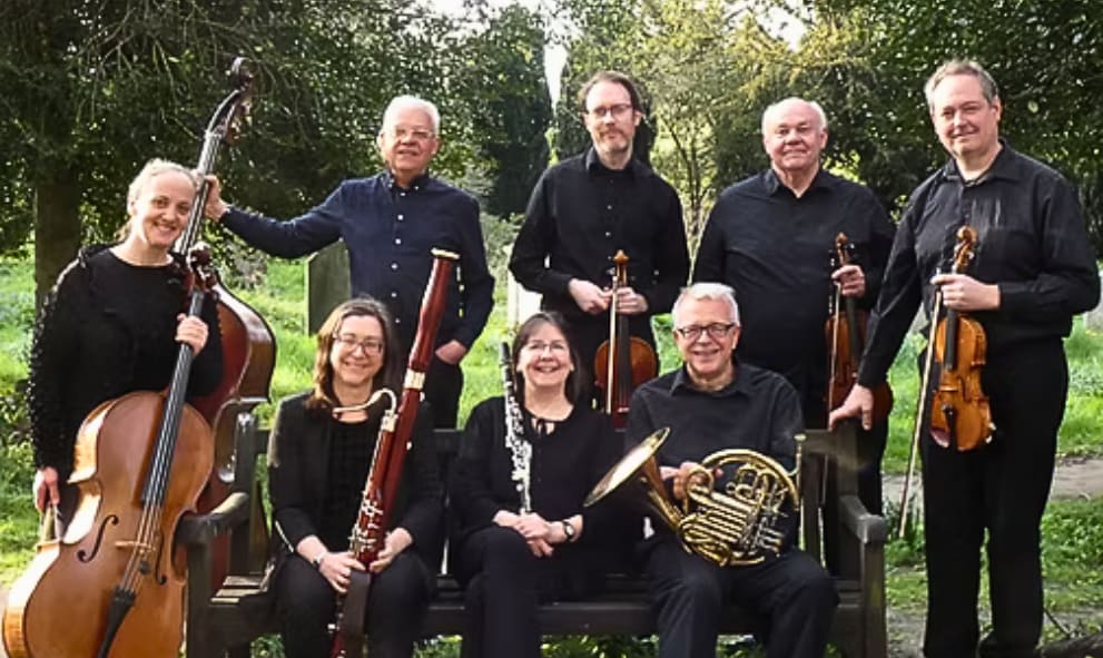 Eight Blaze Ensemble musicians pose for a group photo with their instruments (cello, three violins, oboe, french horn, clarinet)