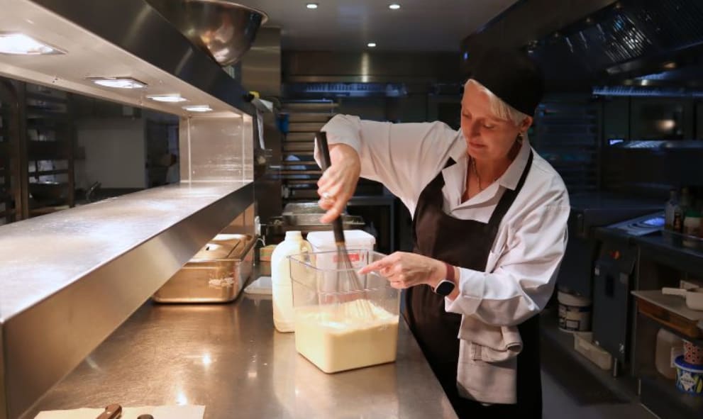 Emma Hopkins whisking custard in chefs whits with a blakc hat and apron in the Lincoln's Inn kitchen