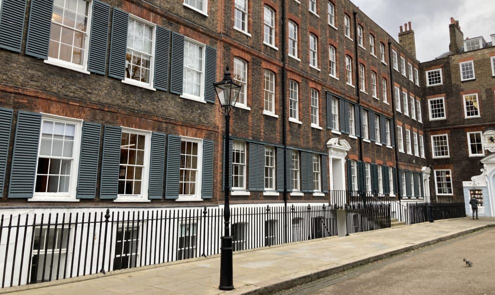 Long row of historic brick buildings with white-framed windows and blue shutters under a cloudy sky.