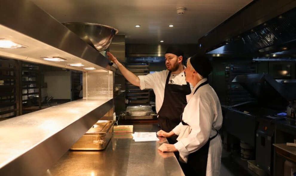 Emma Hopkins in chefs whites is shown around the Lincoln's Inn kitchen