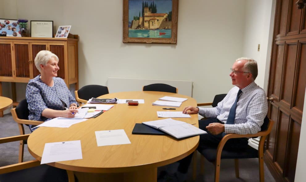 Under Treasurer meets Treasurer. They are sitting at a wooden desk covered in paperwork