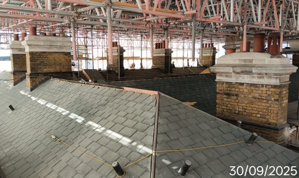 Rooftop under scaffolding, showing brick chimneys and grey slate tiles. The scene conveys an ongoing restoration. Date stamp reads 30/09/2025.