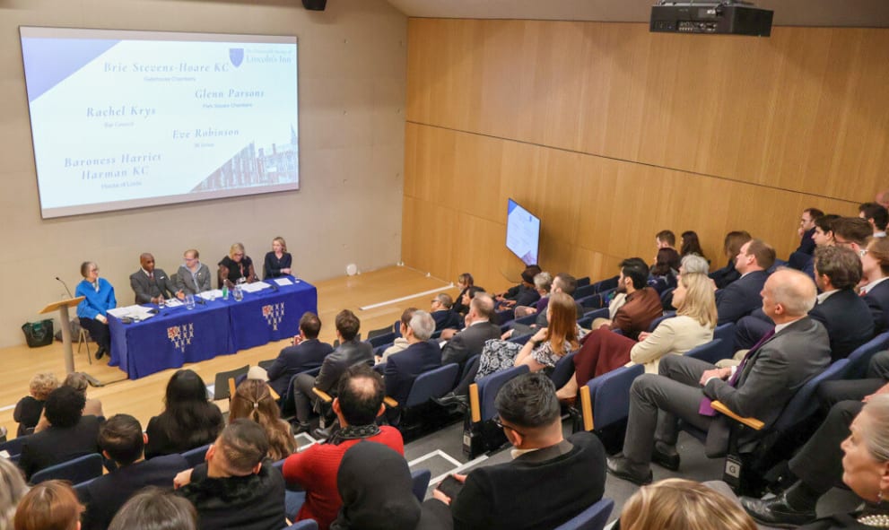 Lecture theatre of attendees listen to panellists in discussion with Baroness Harriet Harman KC