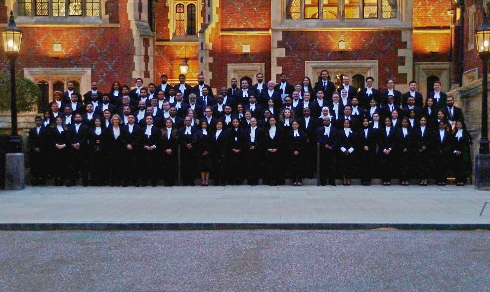 Large group of formally dressed individuals posing in front of a historic brick building at dusk.