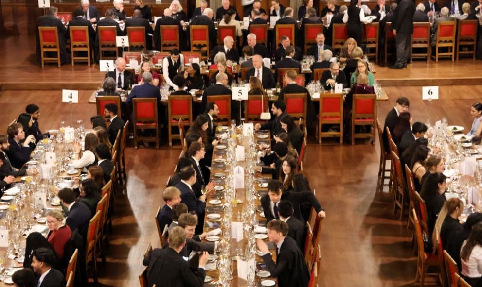 Inn members and guests in professional attire and gowns, dining at mess tables in Great Hall