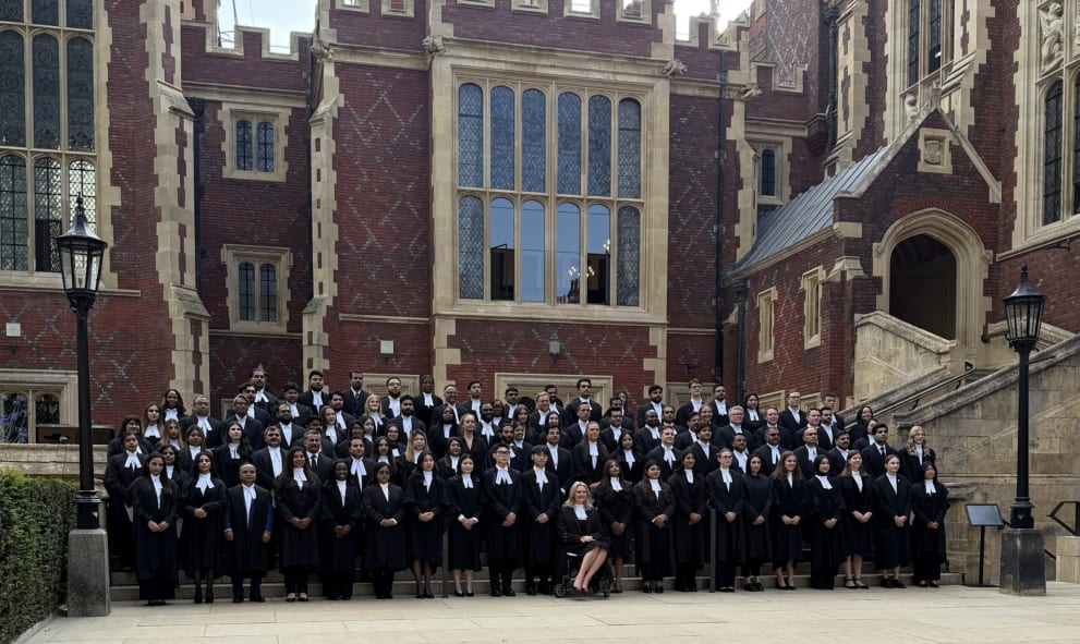 A group of around 100 newly called barristers (on 23 July), in professional attire, long black gowns, and white collars, pose for a group photo on the steps of Lincoln's Inn, in front of a large red brick Victorian building