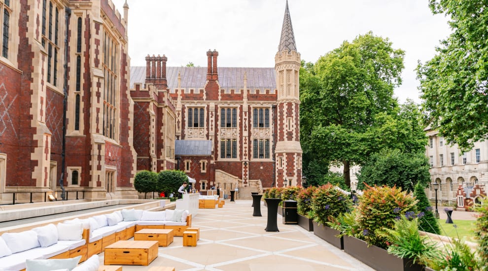 A photo of a terrace at Lincoln's Inn with the Great Hall exterior as the backdrop. The terrace has wooden soft seating and is surrounded by greenery