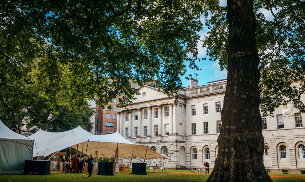 A Summer reception on the North Lawn of Lincoln's Inn estate featuring a stretched tent surrounded by london plane trees and stone buildings as a backdrop.