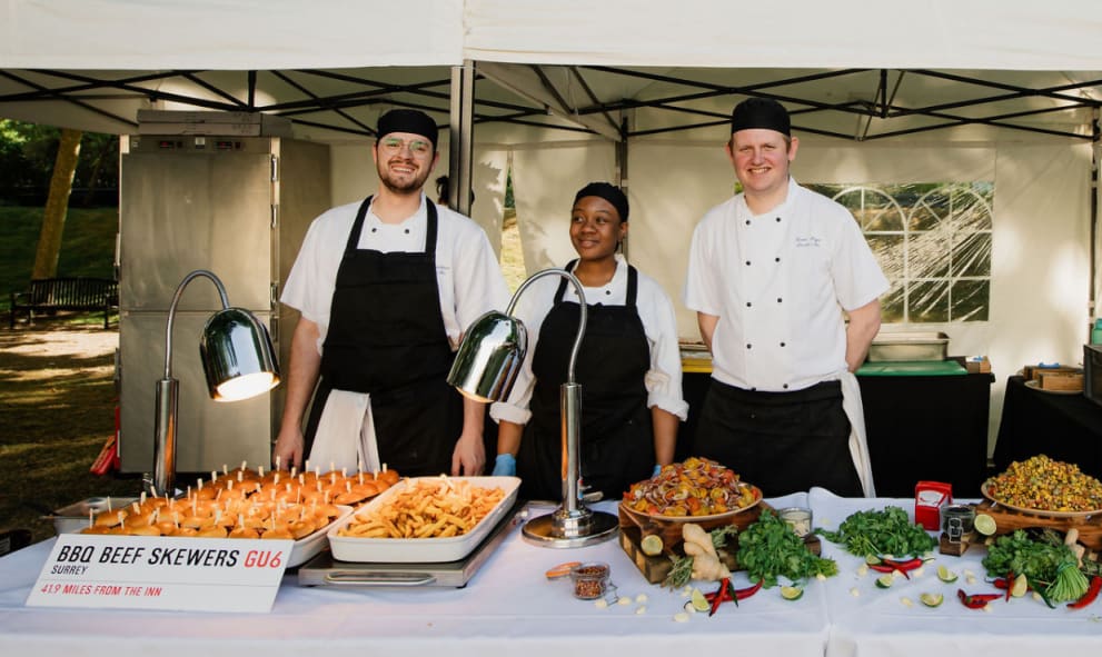 3 Chef's at a garden party food stall standing behind dishes with a sign reading 