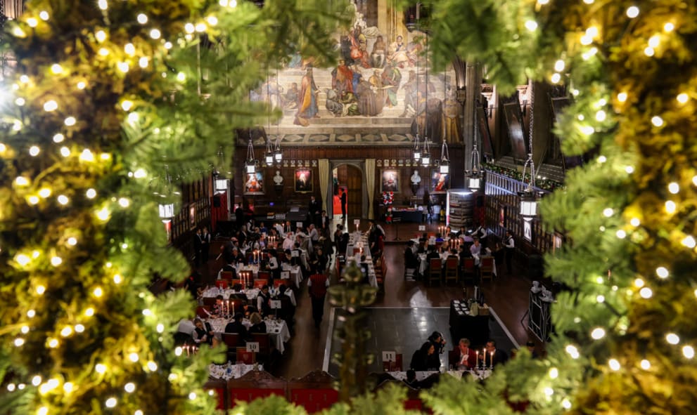 The Great Hall full of guests at a Christmas event - the photo is taken through a fairy-lit Christmas wreath in the minstrel gallery