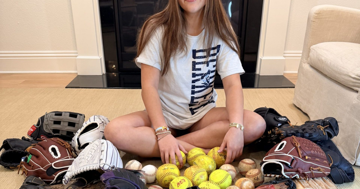 Young girl in softball uniform smiling on baseball field with new multi-use complex behind her