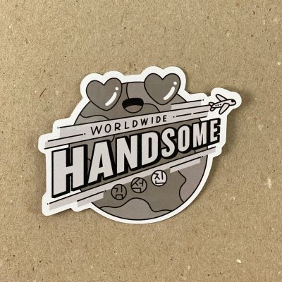 Illustration of a globe with heart eyes and hand drawn text across saying: Worldwide Handsome. Kim Seokjin is written in Korean in 3 circles below the main text. This sticker is black and white tones