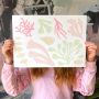 Artist holding collage inspired by the plants and flowers that you find under the sea in soft pastel colours