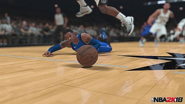 A basketball player dives for a ball on the hardwood as another player jumps