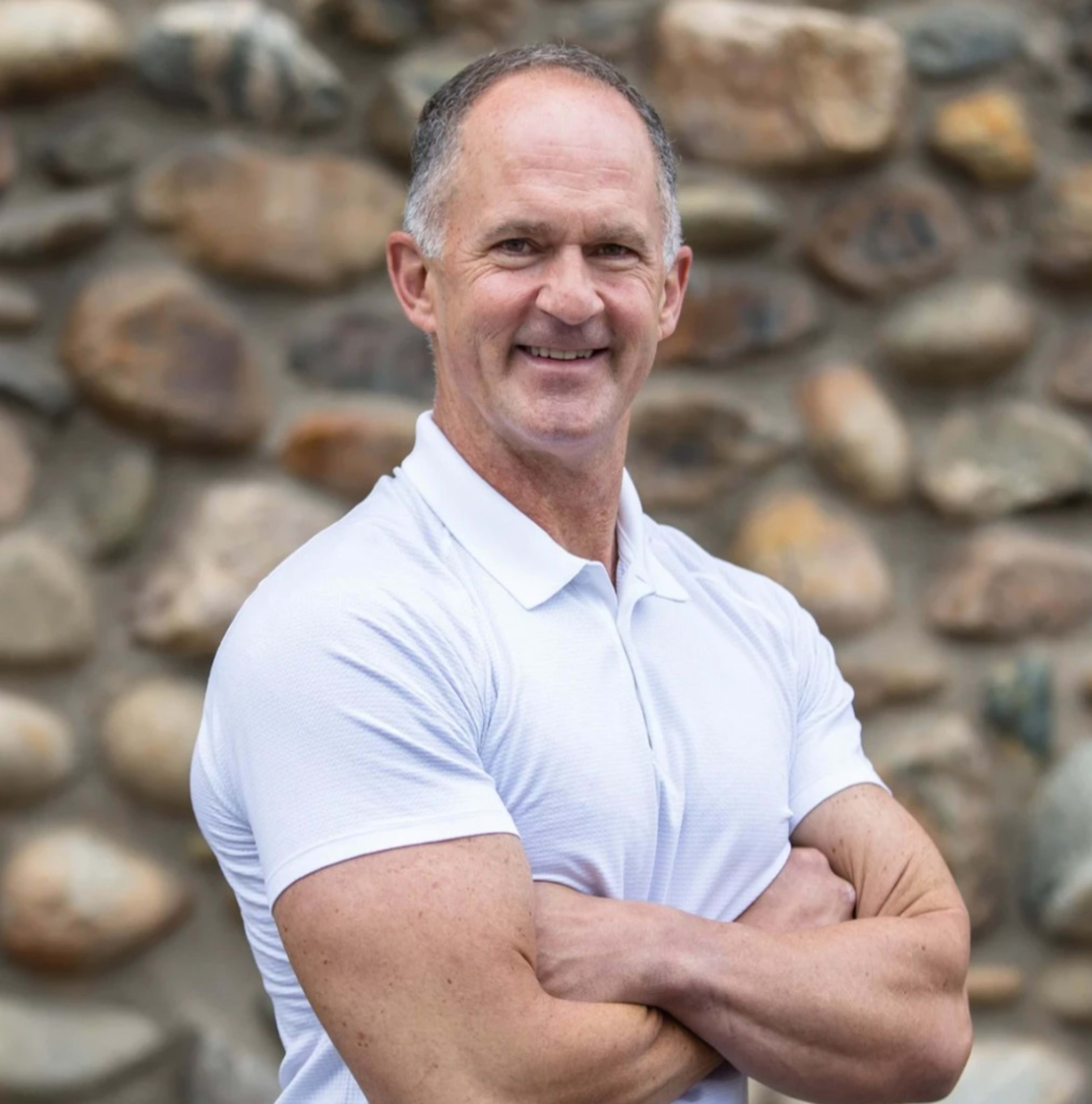 Bill Douglas: fit, arms crossed, at ease. The credibility shot: 61, ~9% body fat, thriving with MS 30 years.
