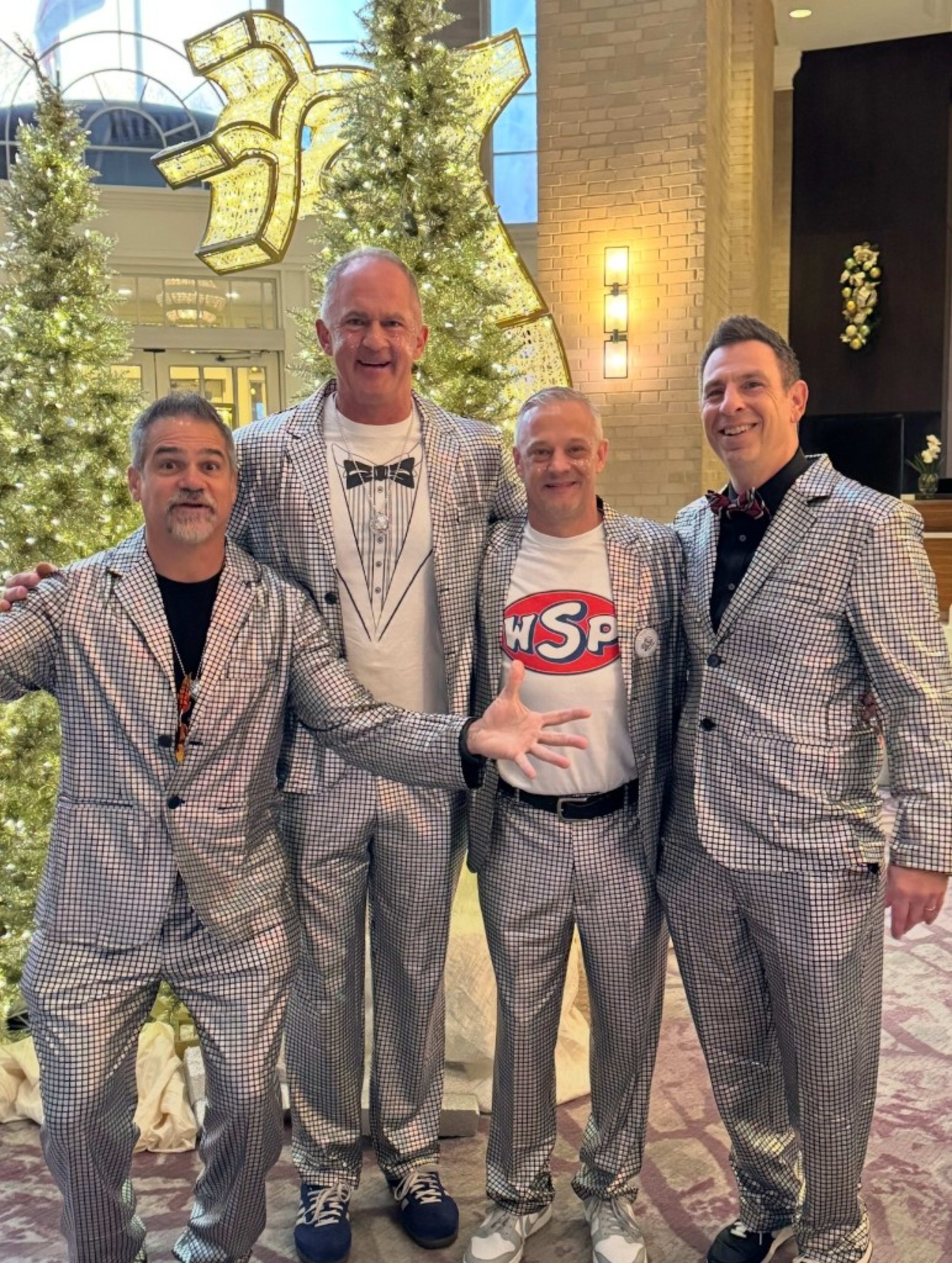 Four friends in matching silver suits at a music weekend, the boys' weekend, nobody taking themselves too seriously.