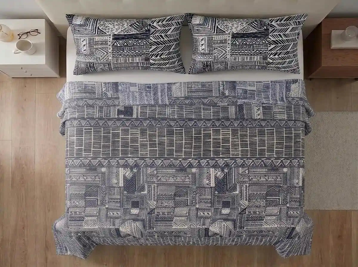 A top-down view of a bed dressed in a black and white geometric tribal patterned bedding set, including a duvet cover and two matching pillowcases, set in a bedroom with light wood floors and bedside tables.